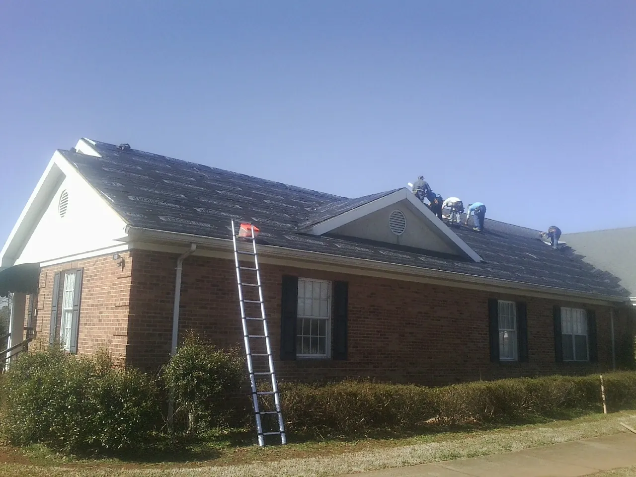 Crew tearing shingles off a brick ranch roof with a ladder set — Metal Roof Repair work by our crew in Juliaetta
