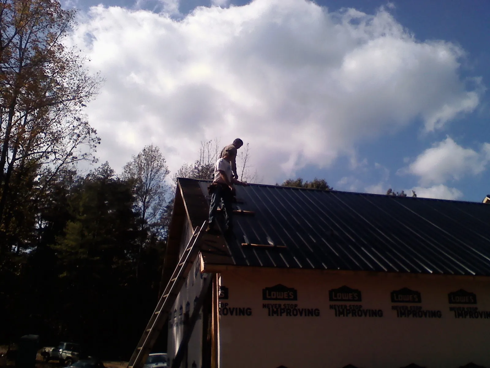 Roofer fastening dark metal panels high against a cloudy sky, from a Roof Inspection job in Juliaetta