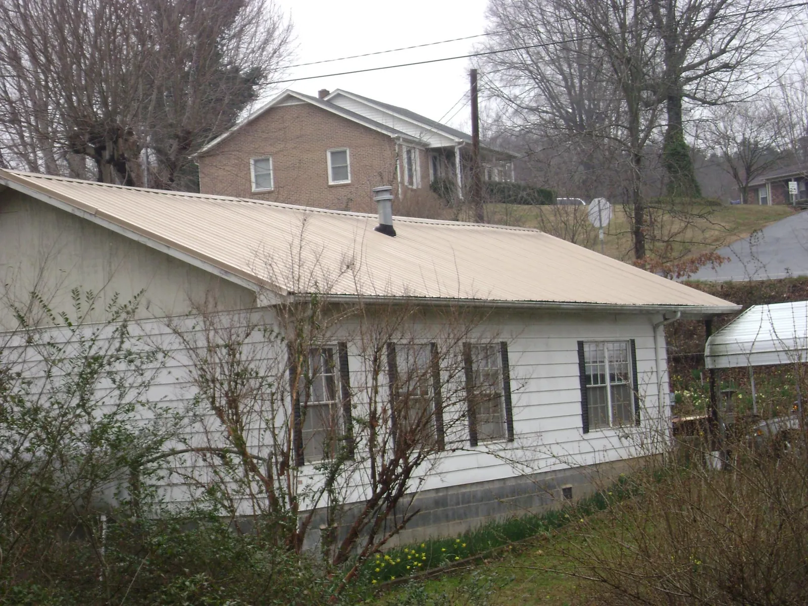 Tan metal roof on a white sided house set into a hillside — Commercial Roofing by Roofing Brothers in Juliaetta