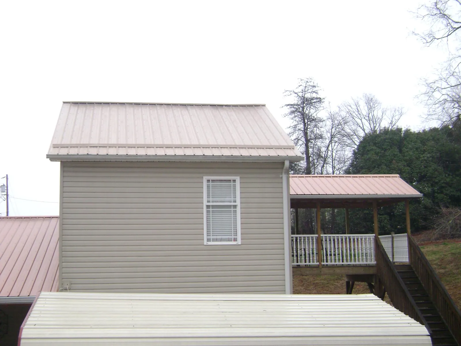 Tan metal roofs on a two story addition and attached porch, from a Roof Replacement job in Juliaetta